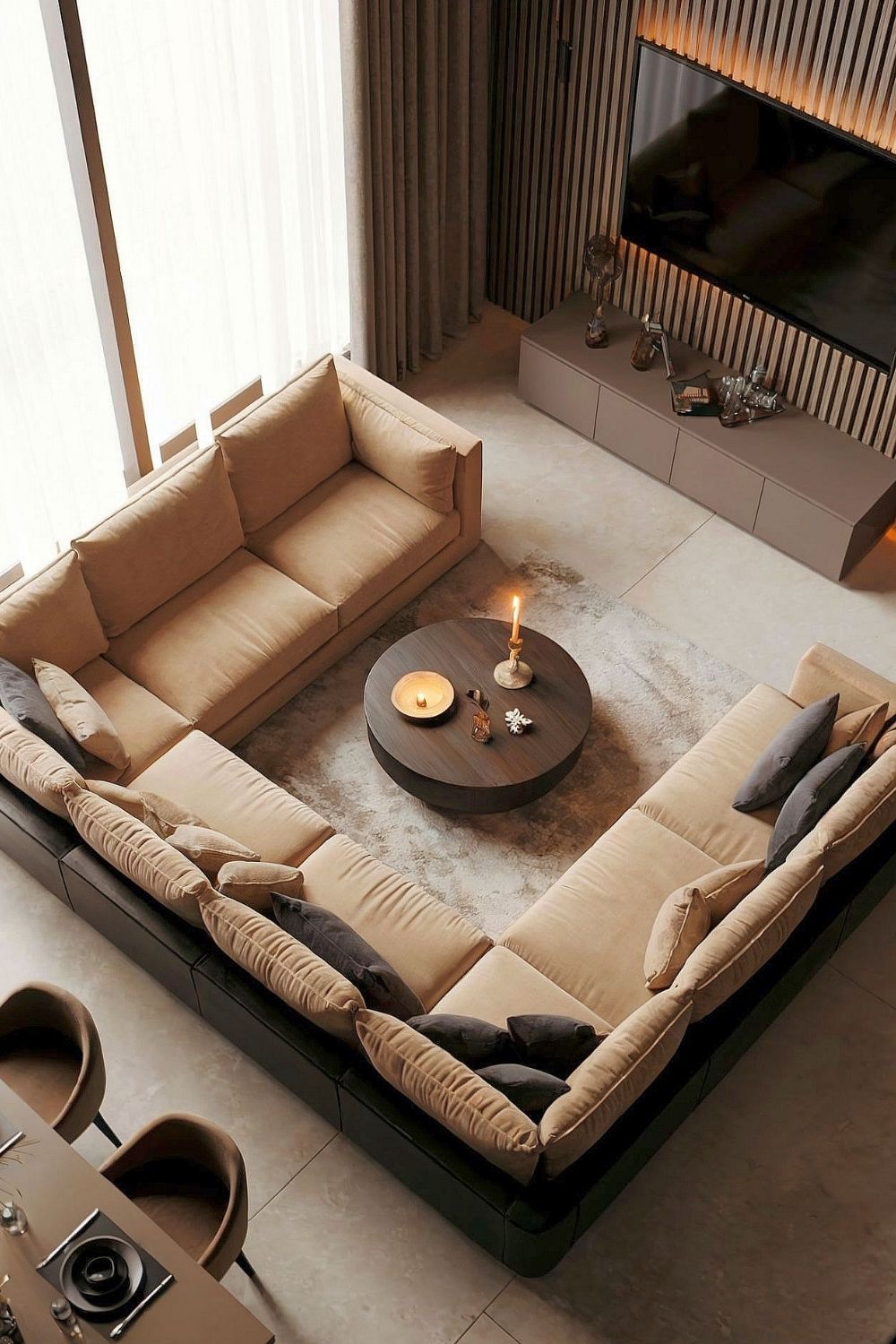 Modern eingerichtetes Wohnzimmer mit einer großen, beigen Sofalandschaft, dunklen Dekokissen, einem runden Couchtisch mit Kerzen, einer stilvollen Holzverkleidung an der Wand und indirekter Beleuchtung für eine gemütliche Atmosphäre sowie elegantes Interieur.