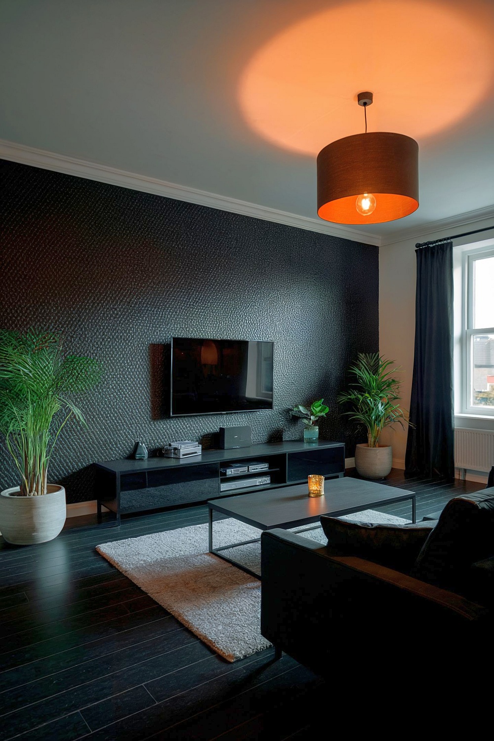 Ein elegantes schwarzes Wohnzimmer mit schwarzer Einrichtung, stilvollen Möbeln und grünen Pflanzen.