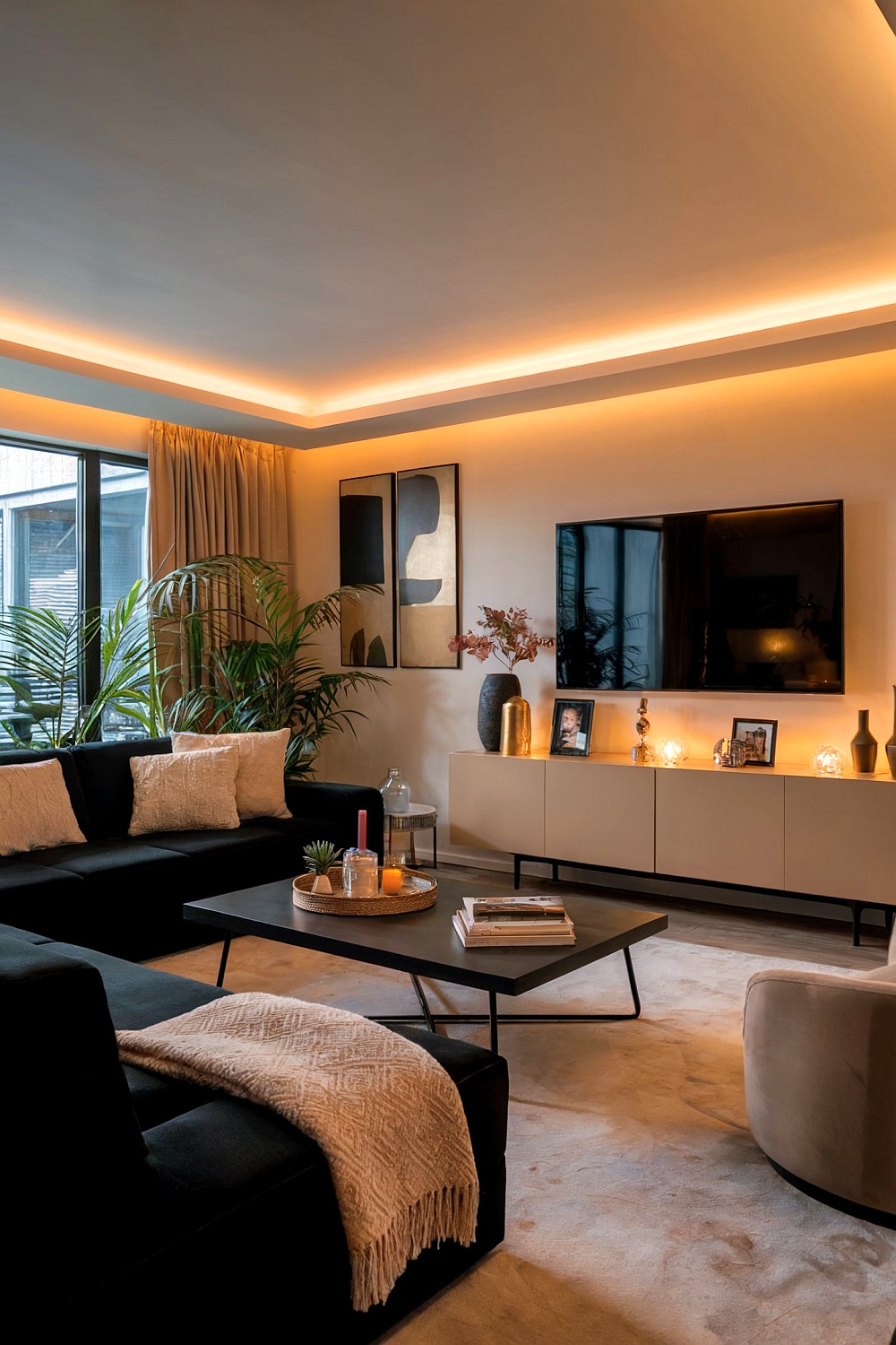 Modernes Wohnzimmer mit einem schwarzen Sofa, umgeben von stimmungsvollem Licht, Pflanzen und modernen Kunstwerken.