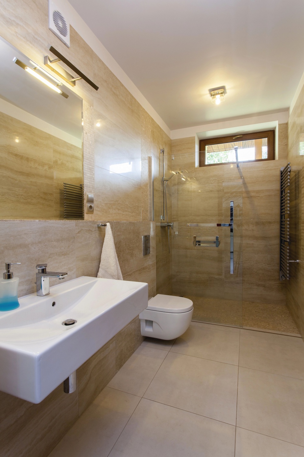 Modernes Badezimmer in Beige mit sandfarbenen Fliesen, begehbarer Dusche, hängendem Waschbecken und Fenster.