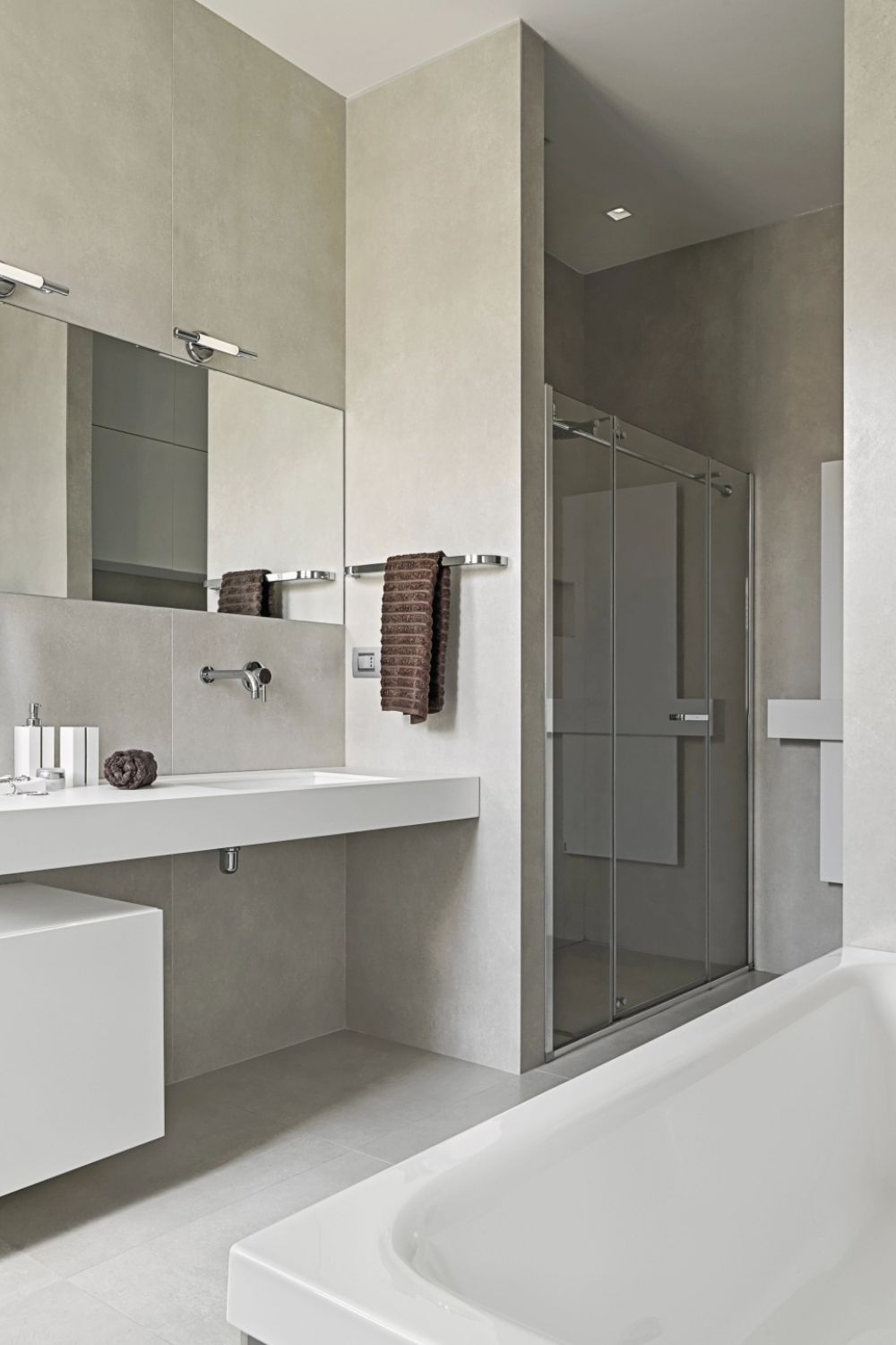 Modernes, minimalistisches Badezimmer mit grauen Wänden, schwebendem weißen Waschtisch, großer Spiegelfläche und Glasdusche.