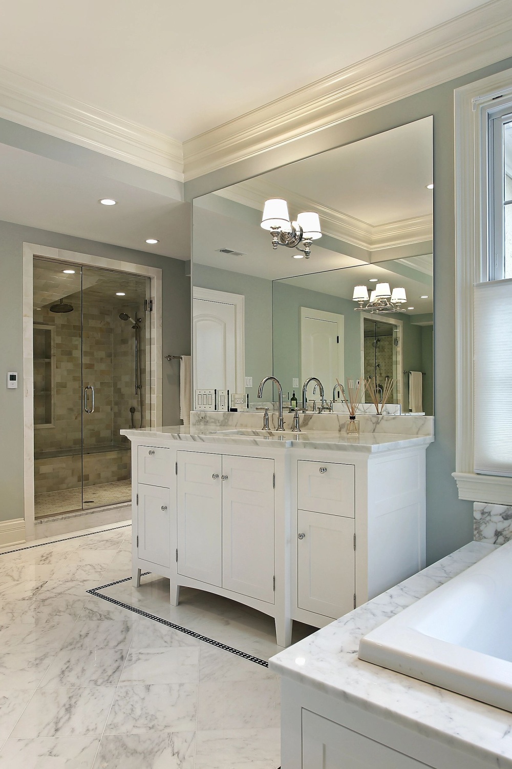 Helles, großes Badezimmer mit großem Waschtisch, Spiegel, Marmorfliesen und geräumiger Dusche.