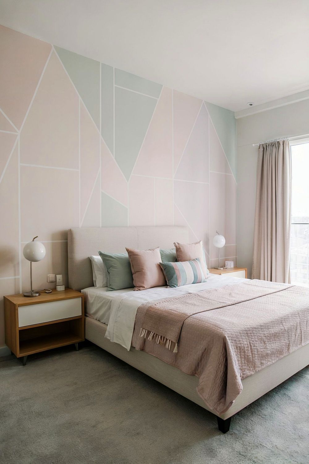 Schlafzimmer mit pastellfarbener Akzentwand in geometrischem Design. Das Bett ist in sanften Beige- und Rosétönen mit gemütlichen Kissen und einer hellen Tagesdecke. Holz-Nachttische mit runden Lampen ergänzen das harmonische Design. Natürliches Licht fällt durch helle Vorhänge ins Zimmer.