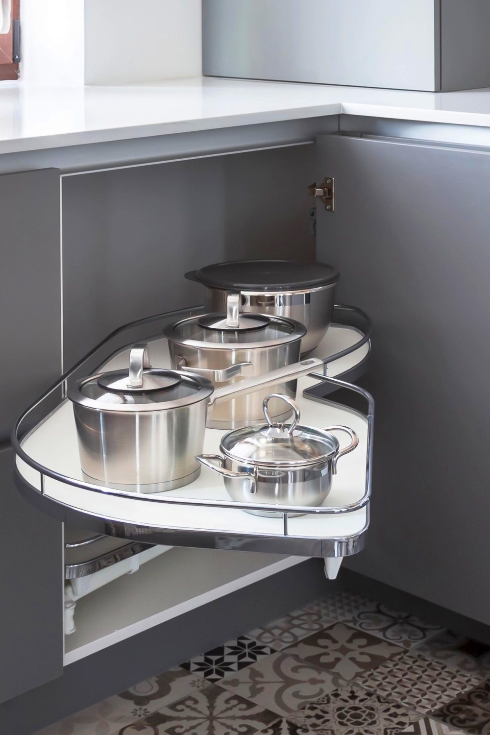 Graue Küchen Ecklösung mit ausziehbarem Schwenkauszug, clever genutzt für Töpfe und mehr, eleganter Fliesenboden mit Muster.