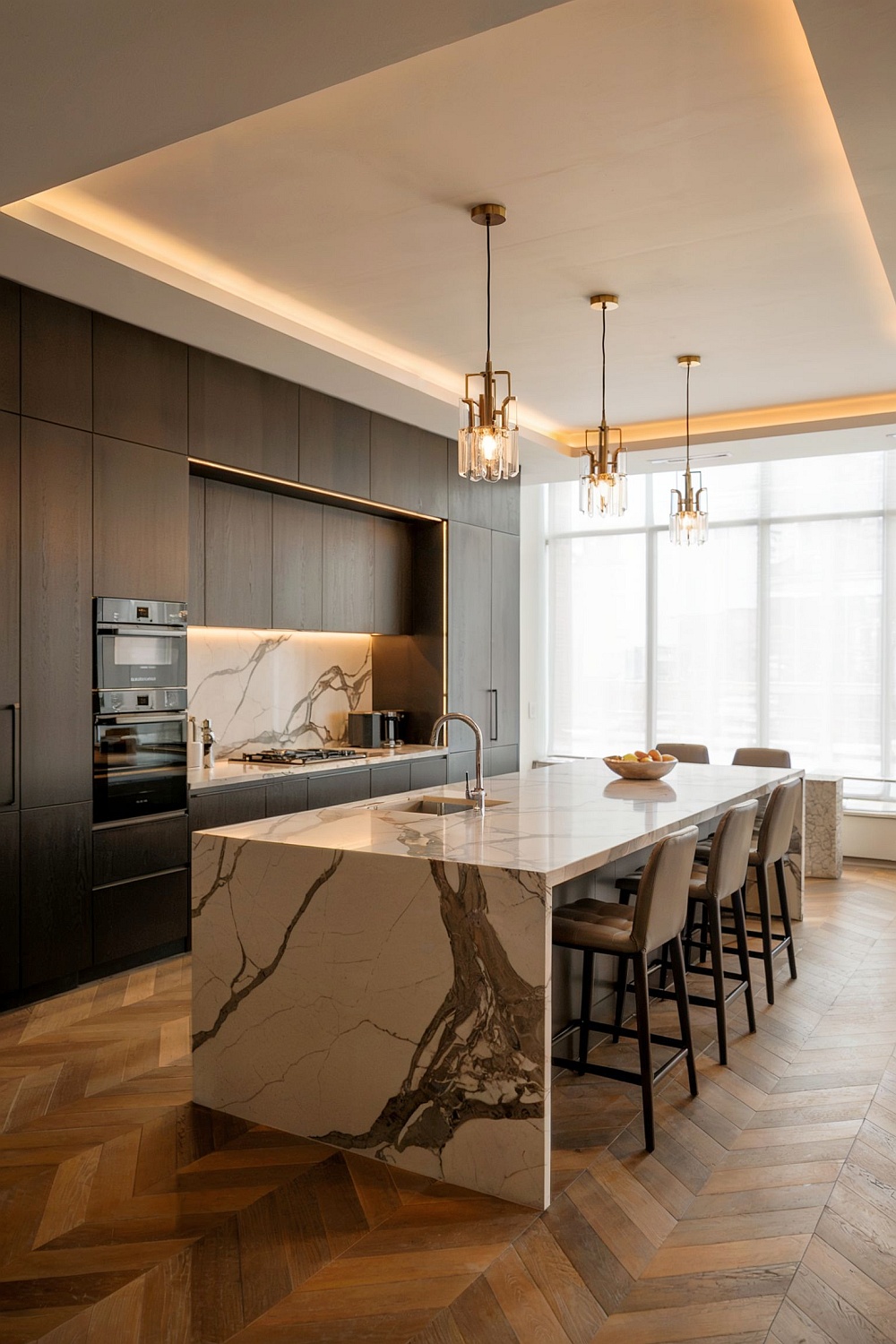 Großzügige Luxus-Küche mit dunklen Schränken, Marmorinsel, elegantem Holzboden und edler Beleuchtung.