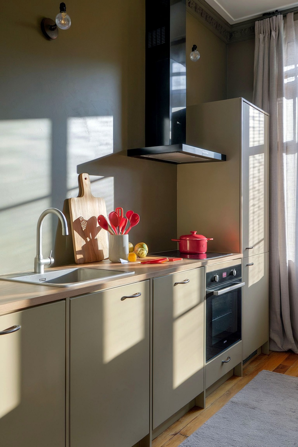 Moderne Küche mit greigen Fronten, Holzarbeitsplatte und roten Akzenten wie Kochutensilien und Topf – minimalistisches Design.