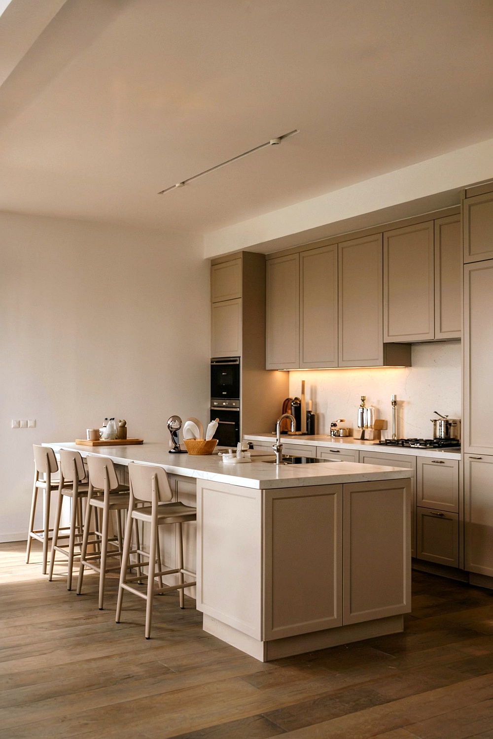 Eine moderne Küche in Taupe mit einer großen Kücheninsel, Barhockern, hellen Arbeitsplatten und integrierten Geräten.