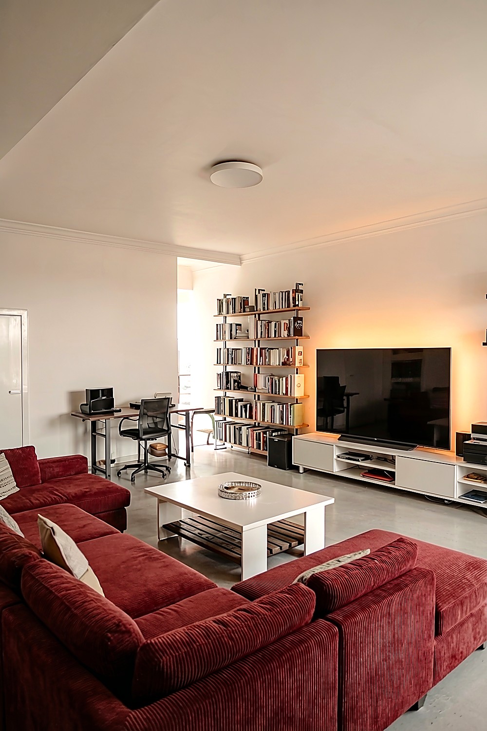 Wohnzimmer mit dunkelrotem Sofa, Couch vor weißem Couchtisch und großem Bücherregal