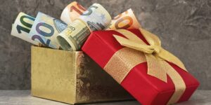 Geldgeschenke zum Geburtstag: gerollte Euroscheine in einer goldenen Geschenkbox mit roter Schleife