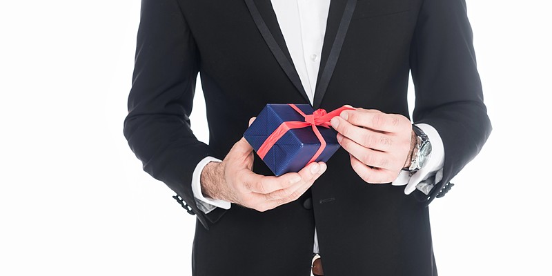 Geschenke für den Freund: Mann im Anzug hält ein blaues Geschenk mit roter Schleife