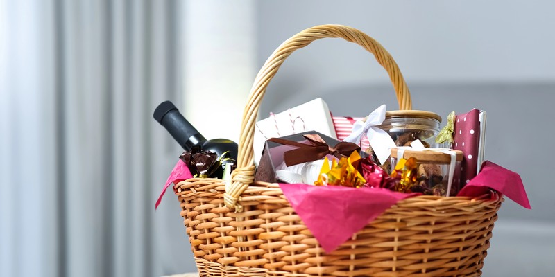 Geschenkkorb selber machen: Weidenkorb mit Wein, Pralinen und Gläsern auf einem Hocker im Wohnzimmer