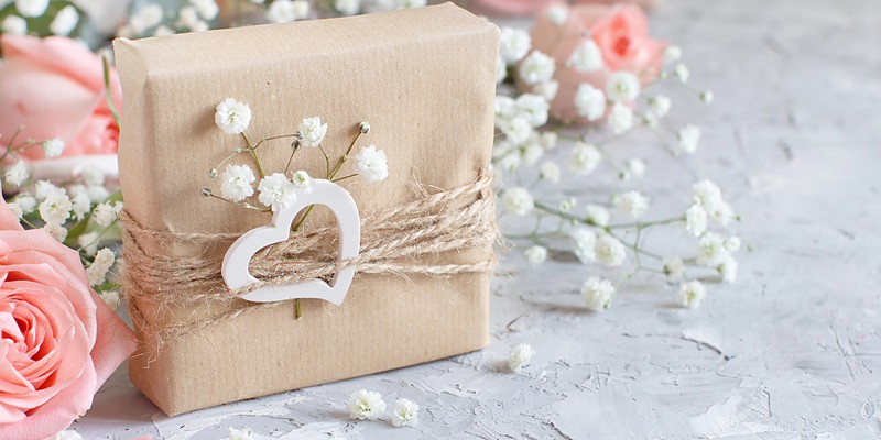 Hochzeitsgeschenke: Päckchen in Packpapier mit Kordel, Holzherz, Schleierkraut und rosa Rosen
