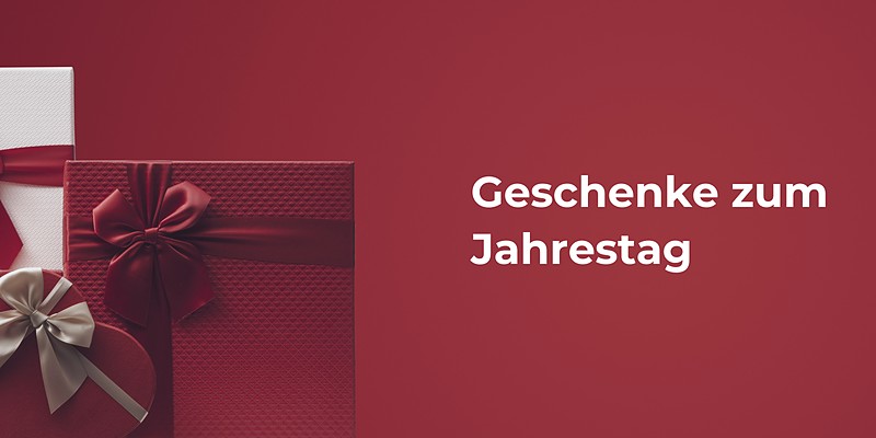 Geschenke zum Jahrestag: rote und weiße Geschenkboxen mit Satinschleifen und eine herzförmige Schachtel vor Rot