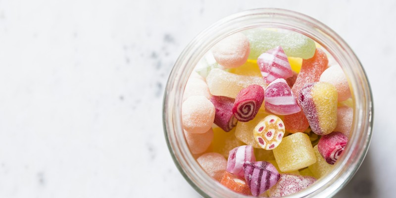 Süßigkeiten als Geschenk: buntes Bonbon-Sortiment in einem Glas auf hellem Marmor