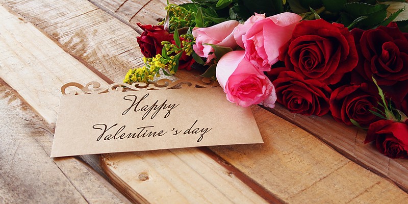 Valentinstag Geschenke: Karte mit Happy Valentine's day neben roten und rosa Rosen auf Holz
