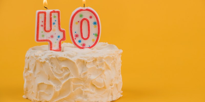 Geschenk zum 40. Geburtstag: weiße Torte mit Zahlenkerzen 40 vor gelbem Hintergrund