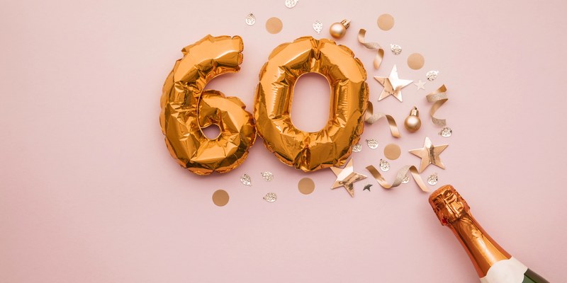 Geschenk zum 60. Geburtstag: goldene Ballonzahl 60 mit Sektflasche und Konfetti auf rosa Grund