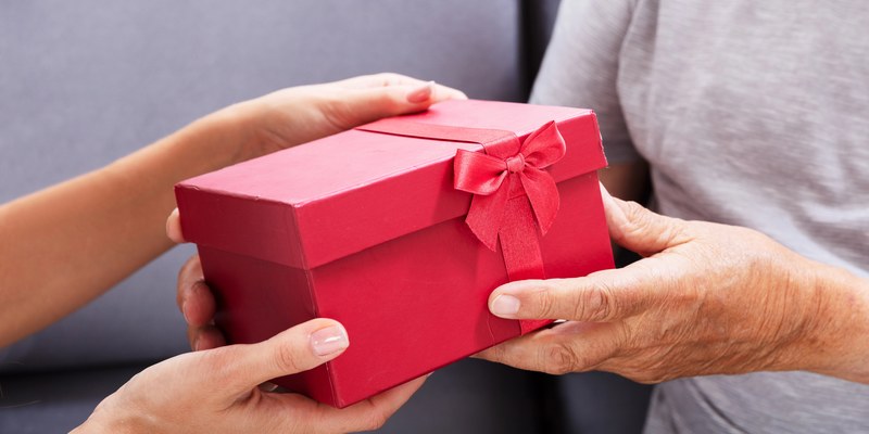 Geschenk zum Ruhestand: zwei Hände überreichen eine rote Geschenkbox mit Schleife