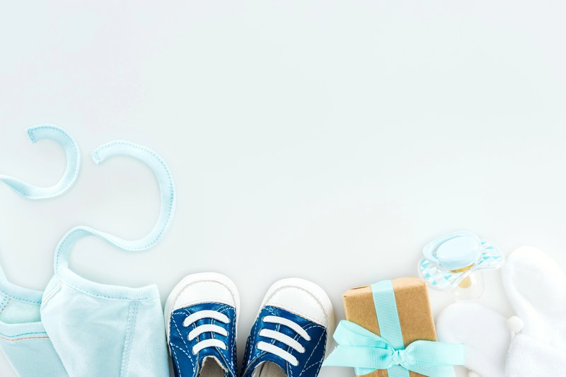 Blaue Babyschuhe, Lätzchen und ein kleines Geschenk mit Schleife auf hellblauem Grund