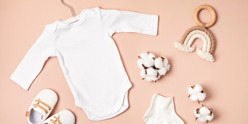 Geschenke zur Geburt: weißer Babybody am Bügel mit Schühchen, Greifring und Baumwollzweigen