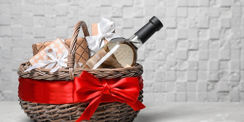 Wein Geschenk: Weidenkorb mit Weinflasche, Gläsern und roter Schleife vor weißer Backsteinwand